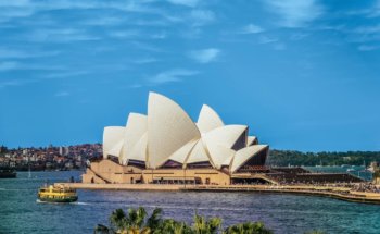 Sydney Opera House with white sails on top and a body of water with a boat in the background
